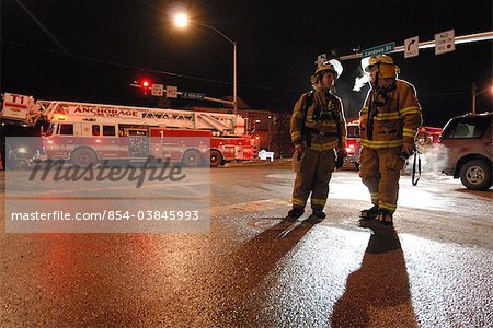 Zwei Feuerwehrmänner in Anchorage Feuerwehr diskutieren Möglichkeiten in einer kalten Winternacht bei der Bekämpfung eines Brandes in King's Court Gebäude nahe der Innenstadt, South Central Alaska, Winter