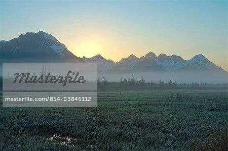 Morning fog hangs on the ground near the Copper River Highway as the sun rise over the Chugach Mountains, Chugach National Forest, Southcentral Alaska, Spring. HDR