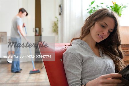 Woman magazine lecture tandis que son mari balaie le sol