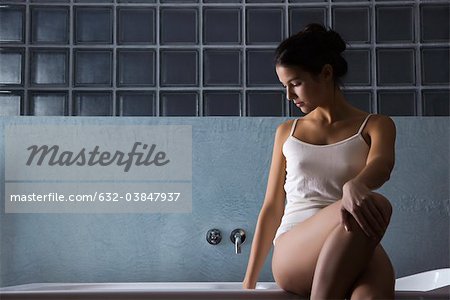 Woman sitting on edge of bathtub in underwear