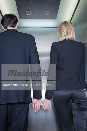 Professionals holding hands in elevator, rear view