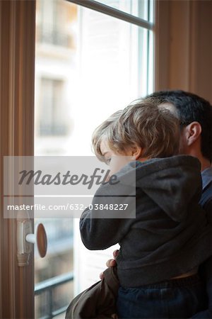 Toddler boy in father's arms, looking out window