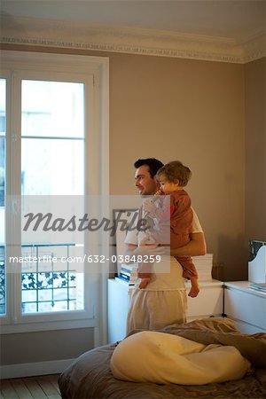 Father holding toddler son, looking out window