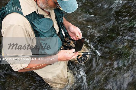 Fly fisherman holding fly case en rivière