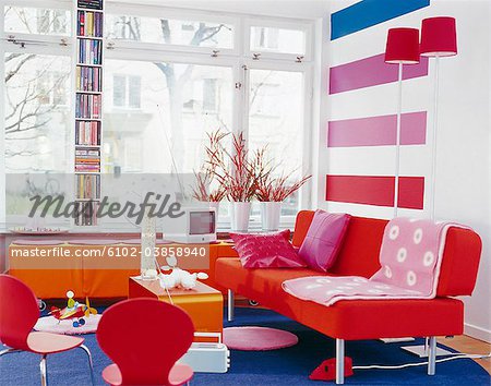 Interior of modern living room with red sofa, chairs, and bookshelf
