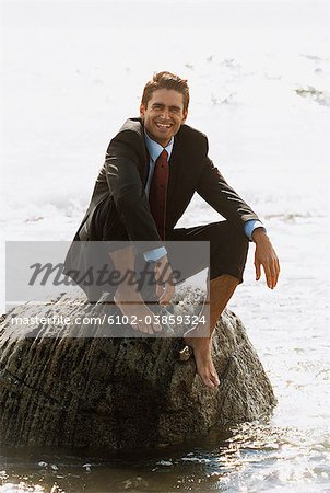 Portrait of barefoot businessman sitting on rock in sea