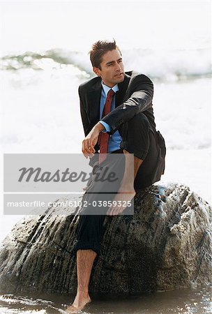 Pieds nus homme d'affaires en costume, assis sur les rochers dans l'eau