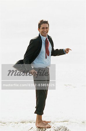 Barefoot businessman standing on rock in sea, laughing