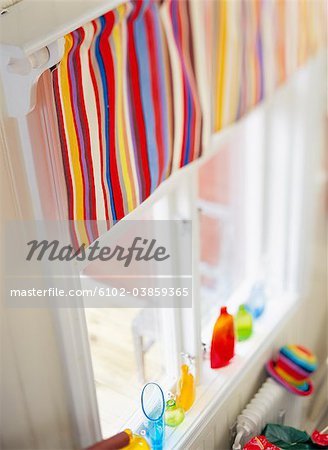 Multi colored vase and bottles on window sill, striped curtain hanging