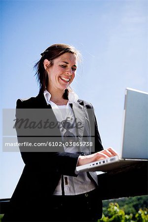 Une femme souriante à l'aide d'un ordinateur portable à l'extérieur, Suède.