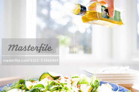 A peson pouring olive oil on a salad, Sweden.