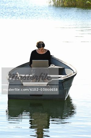 Une femme à l'aide d'un ordinateur portable assis dans un aviron-bateau, archipel de Stockholm, Suède.