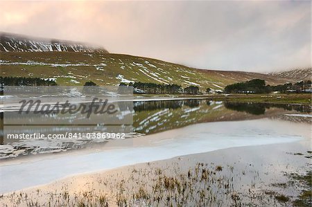 Sunset reflected in the icy waters of the Upper Neuadd Reservoir, with Graig Fan Ddu escarpment in the background in winter, Brecon Beacons National Park, Powys, Wales, United Kingdom, Europe