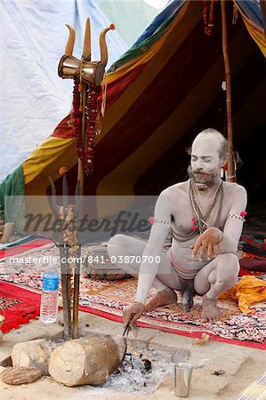 Shivaite Naga sadhu poking a sacred fire in his akhara at the Kumbh Mela in Hardwar, Uttarakhand, India, Asia