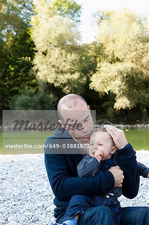 Father holding crying baby by creek