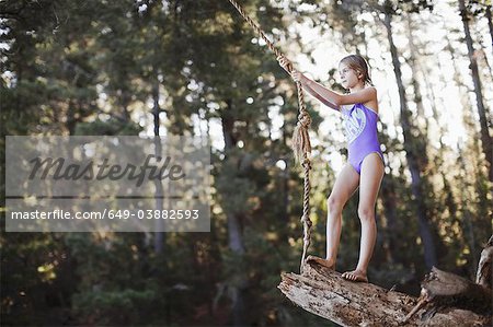 Young girl using rope swing over lake