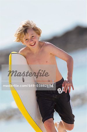Boy carrying surfboard on beach