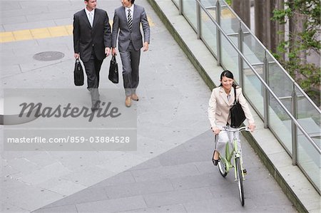 Businesswoman Commuting On Bicycle And Businesspeople Walking