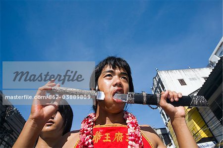 Thailand, Ko Phuket, Phuket.  A Ma-Thong (spirit medium) with cheeks pierced with a sword during the Phuket Vegetarian Festival.   The devotees are believed to possess supernatural powers and perform acts of self-torture to bring the local Chinese community good luck.