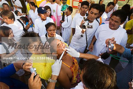 Thailand, Ko Phuket, Phuket.  Crowds watch on as a Ma-Thong (religious devotee) has his cheeks pierced with a metal skewer during the Phuket Vegetarian Festival.    The Ma-Thong are spirit mediums believed to possess supernatural powers and perform acts of self-torture to shift evil spirits from the community onto themselves.