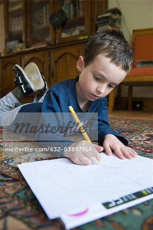 Boy lying on floor, drawing on paper with pencil
