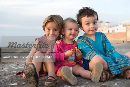 Young siblings sitting together on rocky beach, portrait
