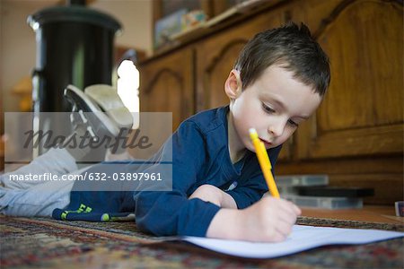 Boy lying on floor, writing on paper with pencil