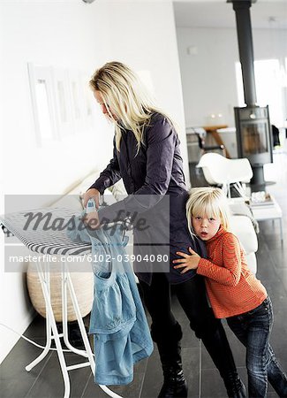 Mother ironing a blouse, daughter hugging her leg, Sweden.