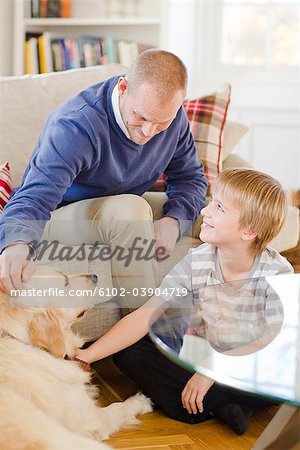 Father and son in a couch patting a dog, Sweden.