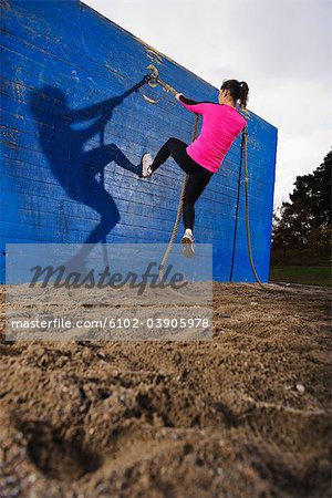 Woman climbing wall using rope in obstacle course