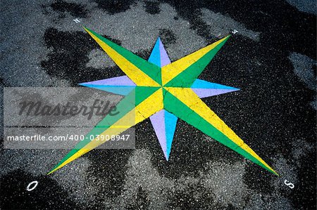 A colourful compass rose set into asphalt, which is slightly wet. Photograph taken in a French-speaking country, which is why west is signified by an 'O' (ouest).