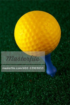 Yellow golfball and blue tee on grass background