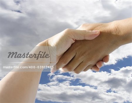 A pair of hands holding or shaking each other against a cloudy background. Concept: Business deal done.