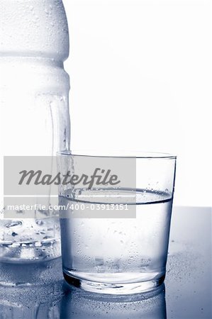 Detail of bottle and glass of mineral water with droplets reflected on white background