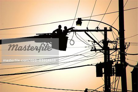 Two utility service workers in a cherry picker working on electrical power lines.