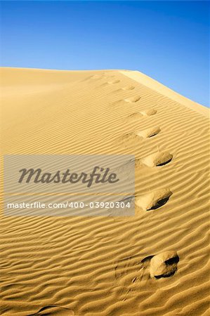 Footprints on sand dune with blue sky
