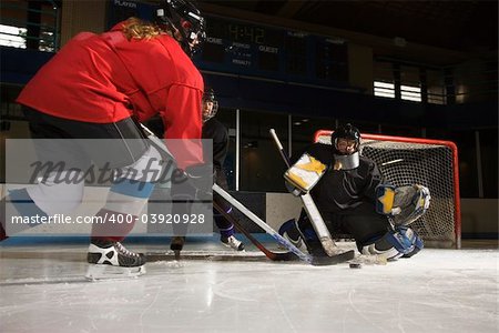 Caucasian female hockey player trying to make goal as goalie protects the net.