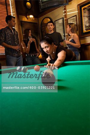 Young caucasian woman preparing to hit pool ball while playing billiards.