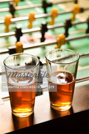 Two glasses of beer on foosball table.