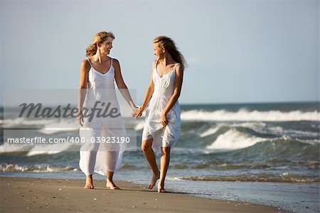 Caucasian mother and pre-teen girl walking on beach holding hands.
