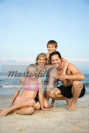 Caucasian family of four posing together on beach.