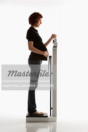 Side view of pregnant Caucasian mid-adult woman reading her weight on scale.