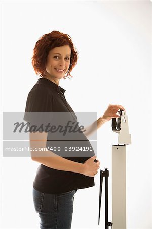 Pregnant Caucasian mid-adult woman standing on scale with head turned toward viewer smiling.