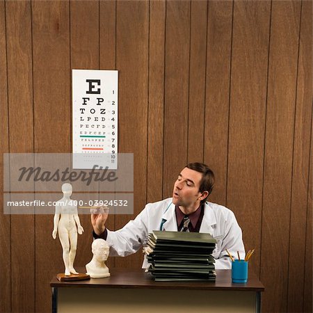 Mid-adult Caucasian male doctor sitting at desk pointing to figurine.