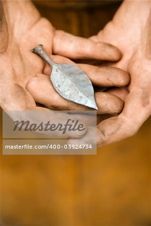 Dirty caucasian male metalmith's hands holding metal leaf.