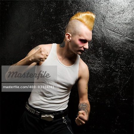 Mid-adult Caucasian male punk with clenched fists looking downward.