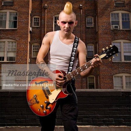 Portrait of a mid-adult Caucasian male punk playing guitar with building in background.