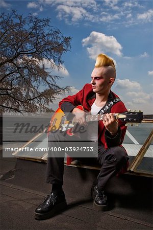 Portrait of a mid-adult Caucasian male punk  sitting on a skylight playing guitar.