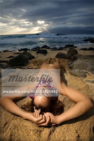 Young Caucasian nude woman wearing lei lying on beach in Maui, Hawaii, USA.