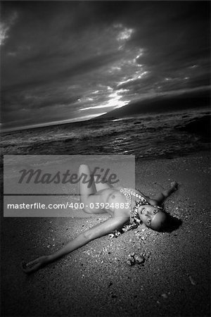 Young Caucasian nude woman wearing lei lying on beach in Maui, Hawaii, USA.